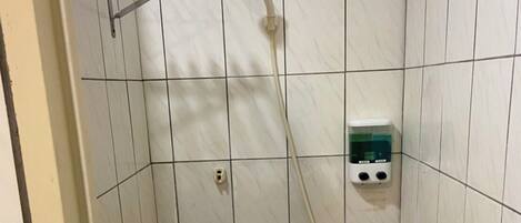 A small, tiled shower room with a handheld showerhead, a soap dispenser, and a metal rack.