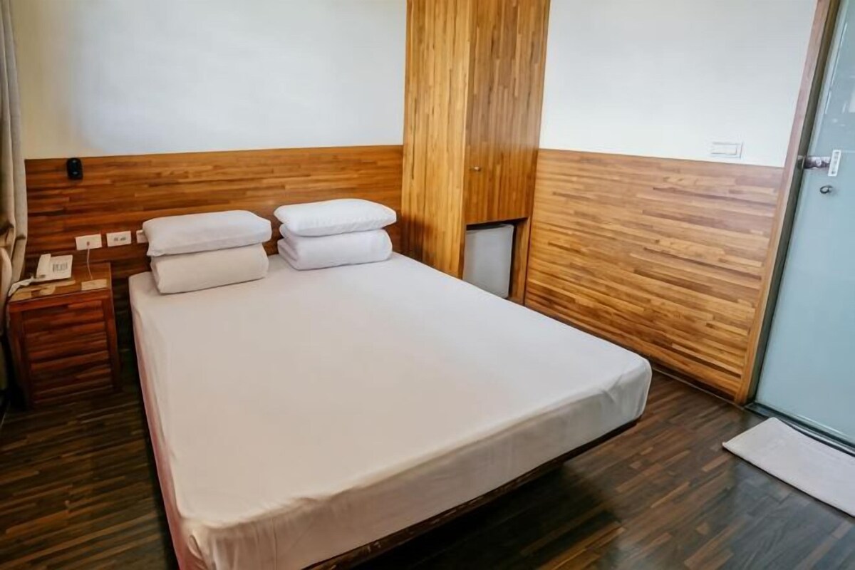 A hotel room with a wooden headboard, a bed with white linens, a nightstand with a phone, and a door to a bathroom.