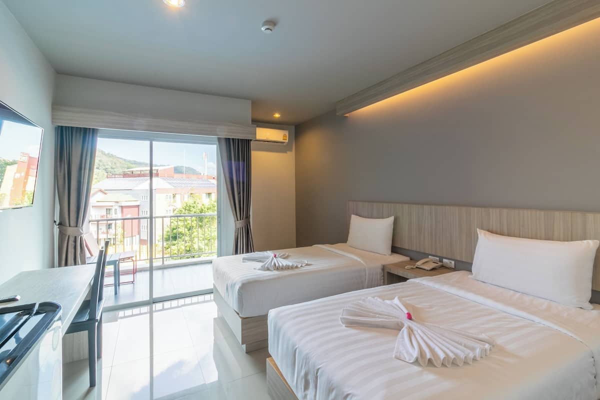A hotel room with two beds, a desk, and a balcony with curtains.