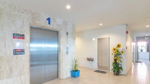A hotel lobby with a marble wall, an elevator, a fitness room sign, and a potted plant with sunflowers. - Carpio Hotel Phuket (Wichit)