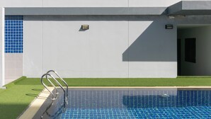 A modern pool area with a clear blue pool, a metal handrail, and a section of artificial grass. - Carpio Hotel Phuket (Wichit)