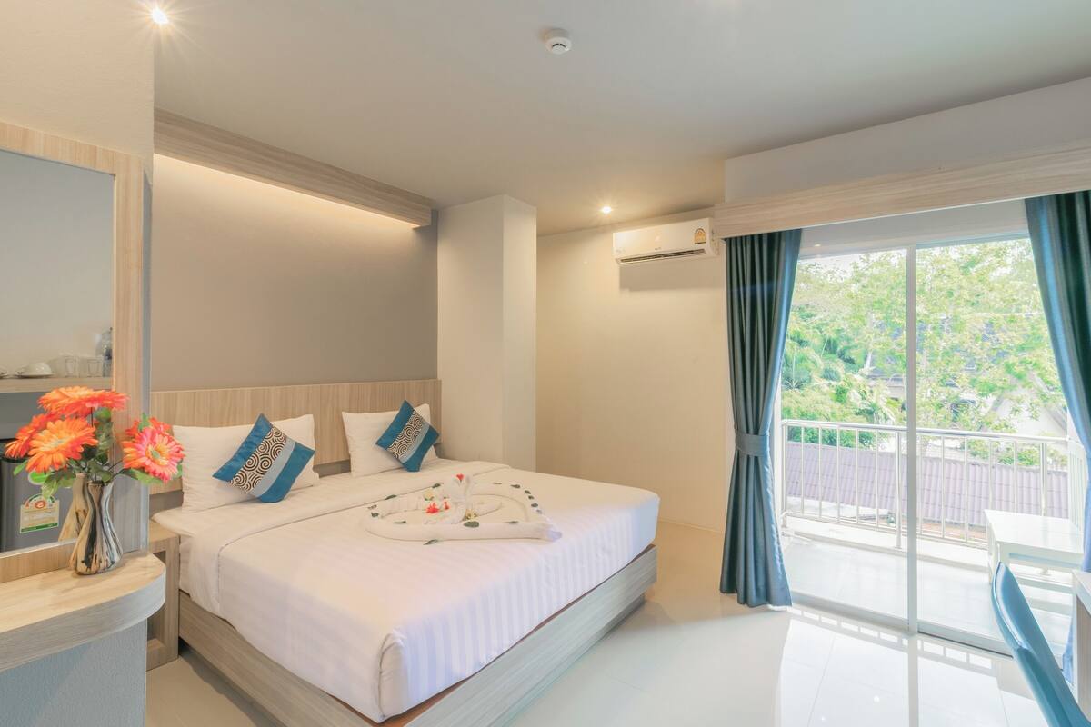 A hotel room with a large bed, a bedside table with a vase of flowers, a window with curtains, and a balcony.
