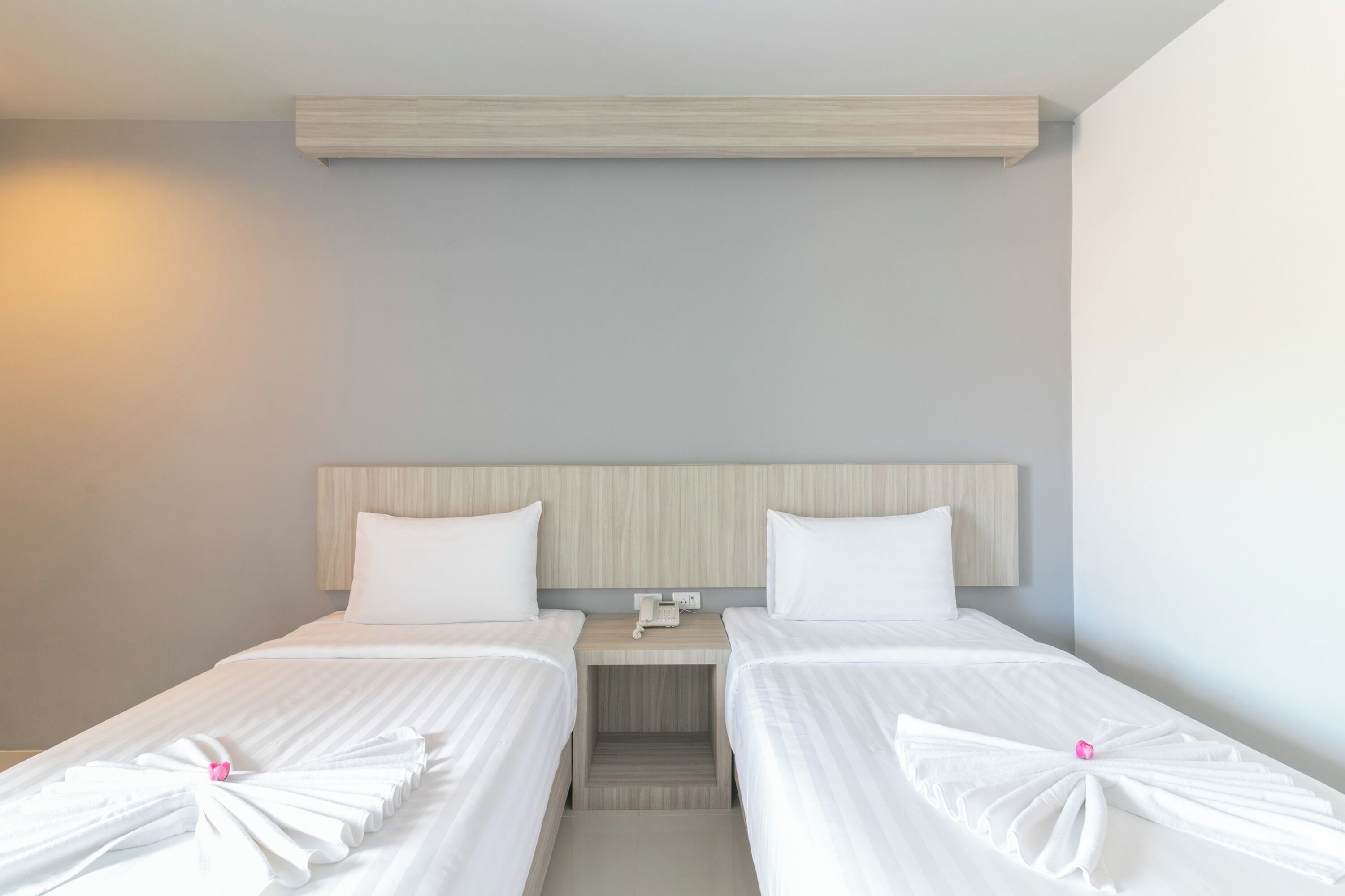 Habitación de hotel con dos camas individuales, cabecera de madera, mesita de noche con teléfono y lámpara de pared.
