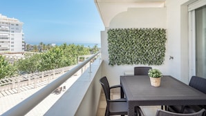 A balcony with a table and chairs, a potted plant, and a green wall. - Apartment with sea view, parking, wifi (Marbella)