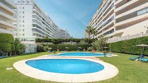 A swimming pool surrounded by a well-maintained lawn, with multiple balconies on adjacent buildings. - Apartment with sea view, parking, wifi (Marbella)