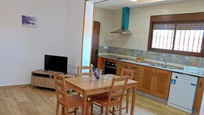 A dining area with a wooden table and chairs, a television, and a kitchen with wooden cabinets and a tiled backsplash. - Villa with private pool and Wi-Fi (CONIL DE LA FRONTERA)
