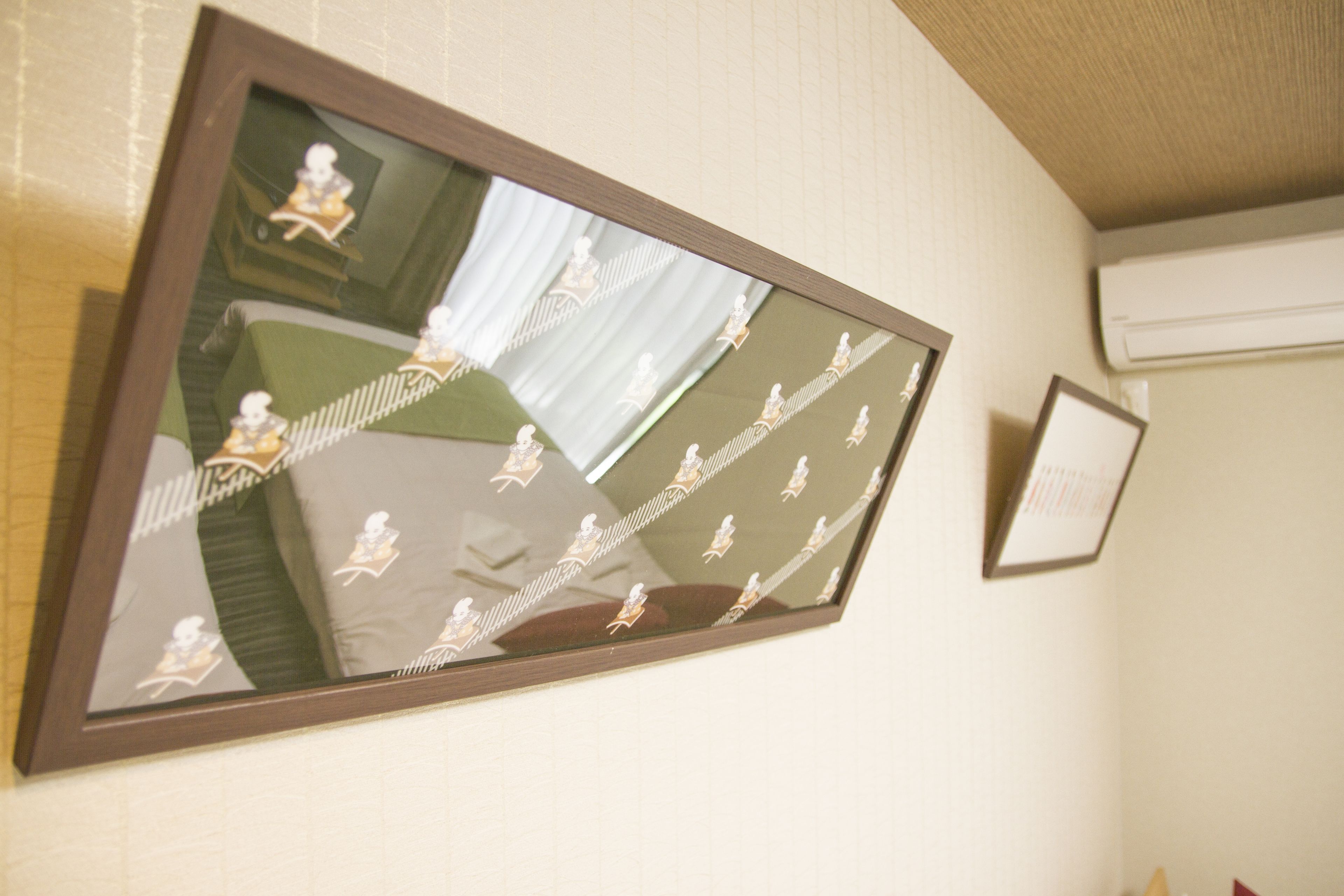 Un espejo en marco que refleja una habitación, un cuadro pequeño en marco y un equipo de aire acondicionado en la pared.