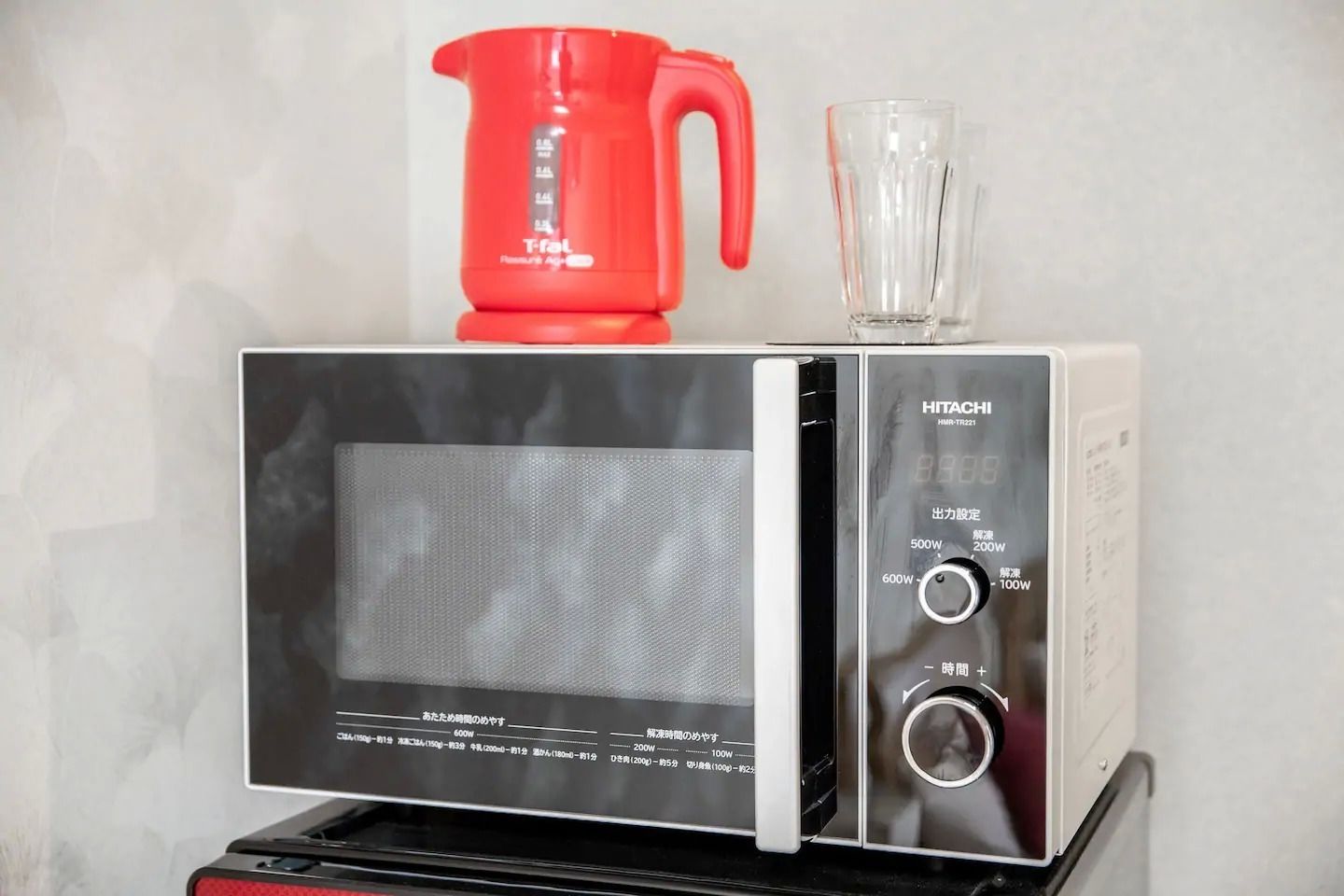 A microwave with a digital display and control panel, placed on a black stand.