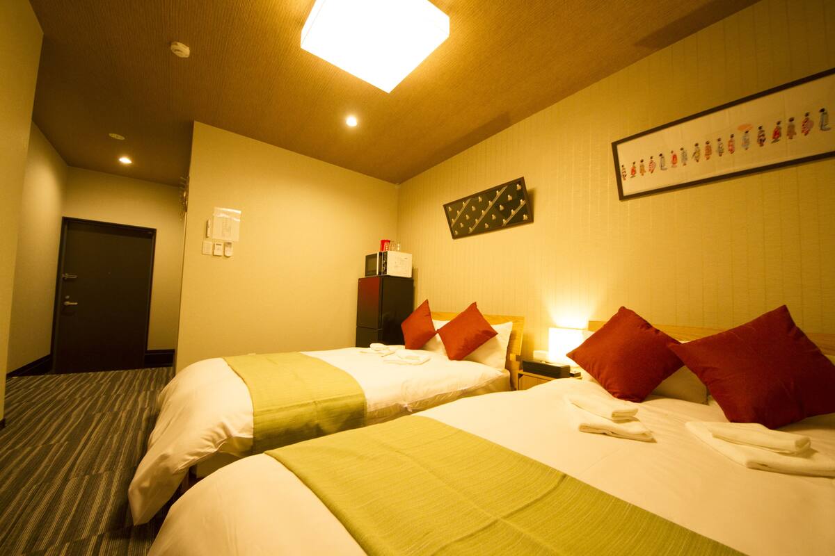 A hotel room with two beds, a microwave, a minibar, and a framed artwork on the wall.