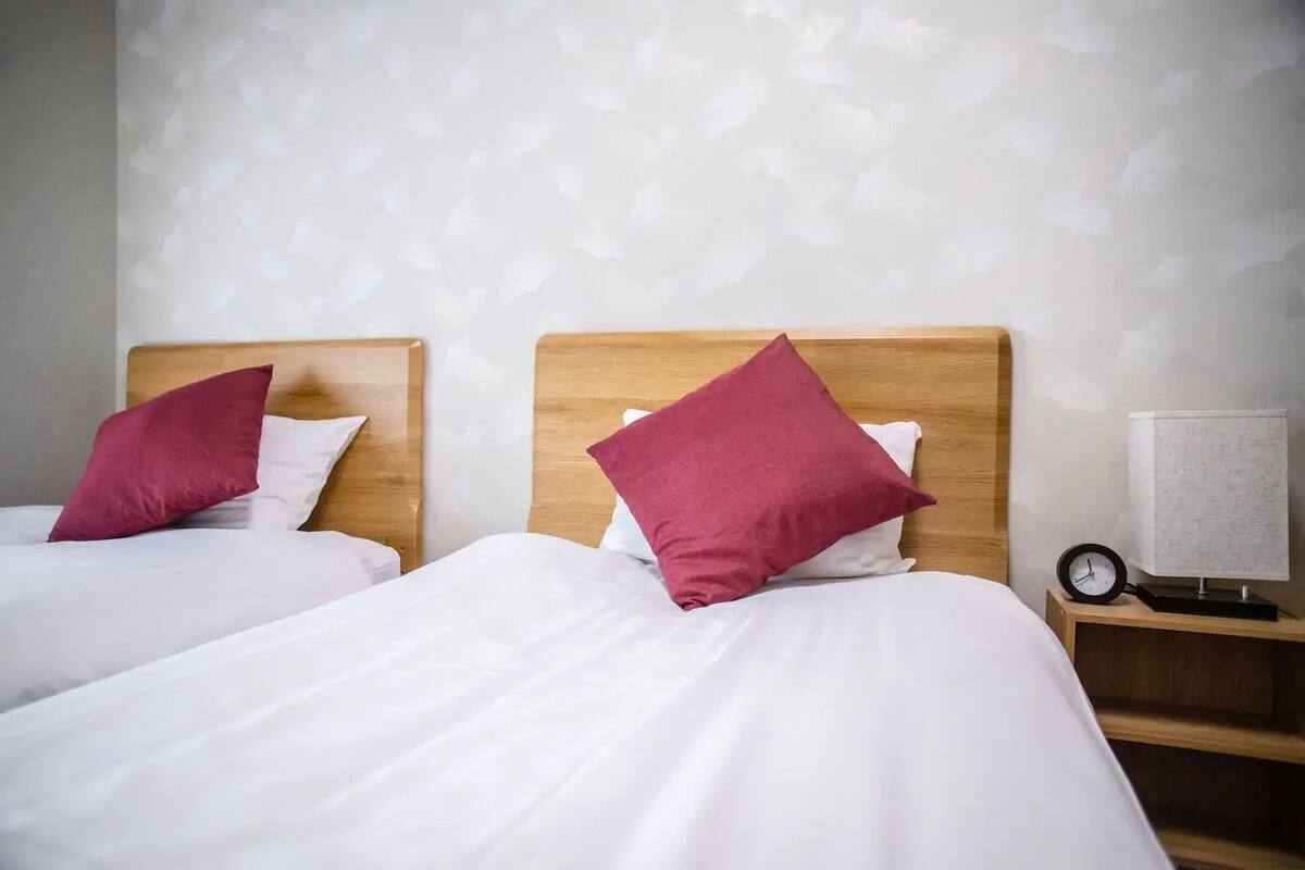 Two beds with wooden headboards and white bedding, a nightstand with a clock and lamp, and a patterned wall.