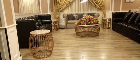 Un amplio espacio de sala con un conjunto de sofás, dos mesas redondas de mimbre y un centro de mesa con flores.