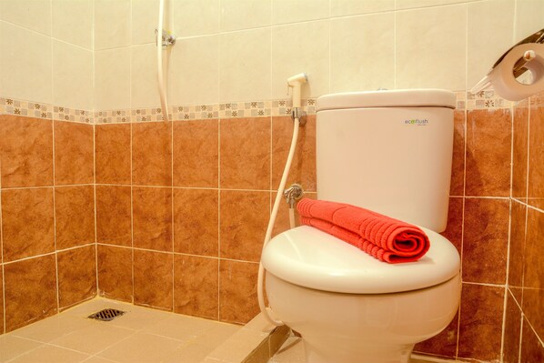A bathroom with a white toilet, a shower, and brown tiles.