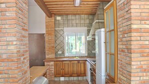 A compact kitchen with a brick wall, wooden cabinets, a window, and a refrigerator. - Villa with private pool and Wi-Fi (CONIL DE LA FRONTERA)