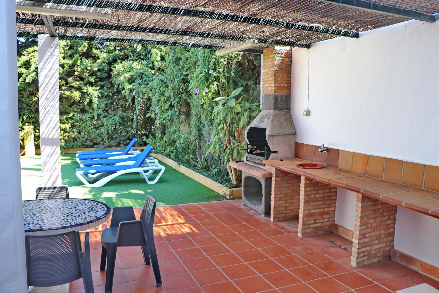 An outdoor patio with a grill, lounge chairs, and a table.