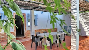 An outdoor patio with a round table and chairs, a brick wall, and a covered area with a thatched roof. - Villa with private pool and Wi-Fi (CONIL DE LA FRONTERA)