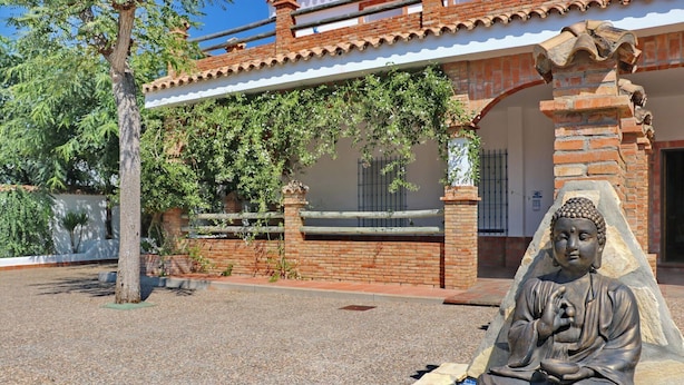 A Buddha statue in a pool, surrounded by a brick wall and a white building with a tiled roof. - Villa with private pool and Wi-Fi (CONIL DE LA FRONTERA)