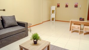 Un salon moderne avec un canapé gris, une petite table en bois ornée d’une plante, une étagère blanche et une table à manger avec des chaises.