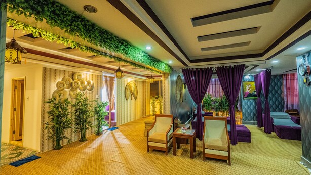 Un hall de hotel con alfombra estampada, un mostrador de recepción y una zona de estar con sillas y una mesa.