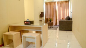 A small, clean room with a desk, two stools, a sofa, and a television. - 3 Bedrooms Plus Apartment Grand Palace by Travelio (Jakarta)