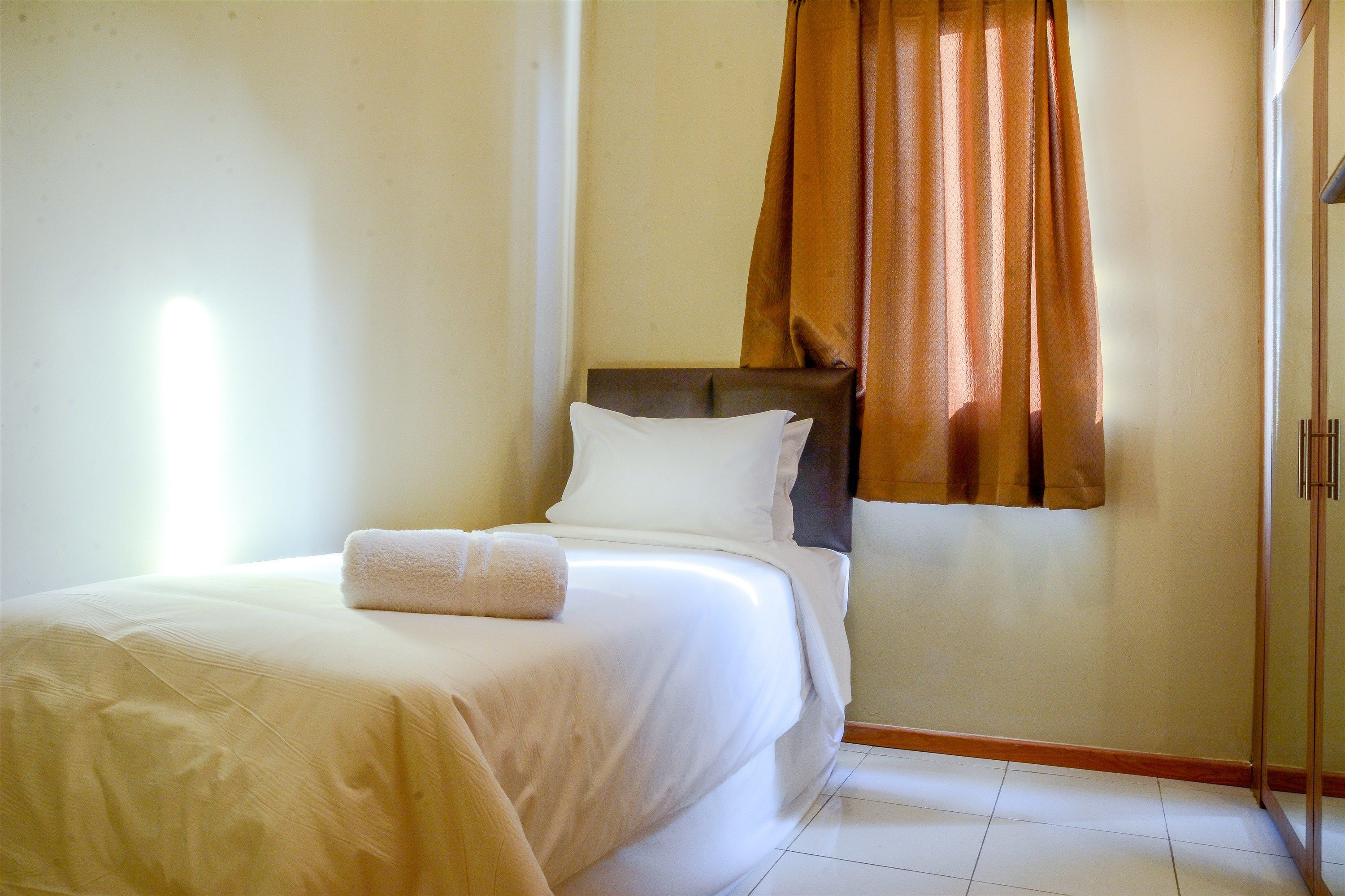 A hotel room with a bed, a headboard, and a window with curtains.