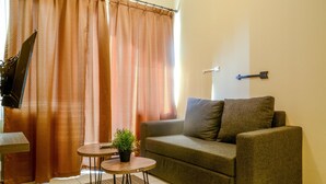 A living room with a sofa, a small table with a plant, and a TV mounted on the wall. - 3 Bedrooms Plus Apartment Grand Palace by Travelio (Jakarta)