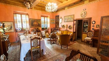 Una stanza con un tavolo da pranzo apparecchiato per quattro persone, circondato da sedie. Un lampadario pende dal soffitto e le pareti sono decorate con quadri e un orologio.