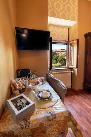 A dining area with a table set for two, a television mounted on the wall, and a window offering a view of buildings and trees. - L'Incontro Residenza Medievale (Viterbo)