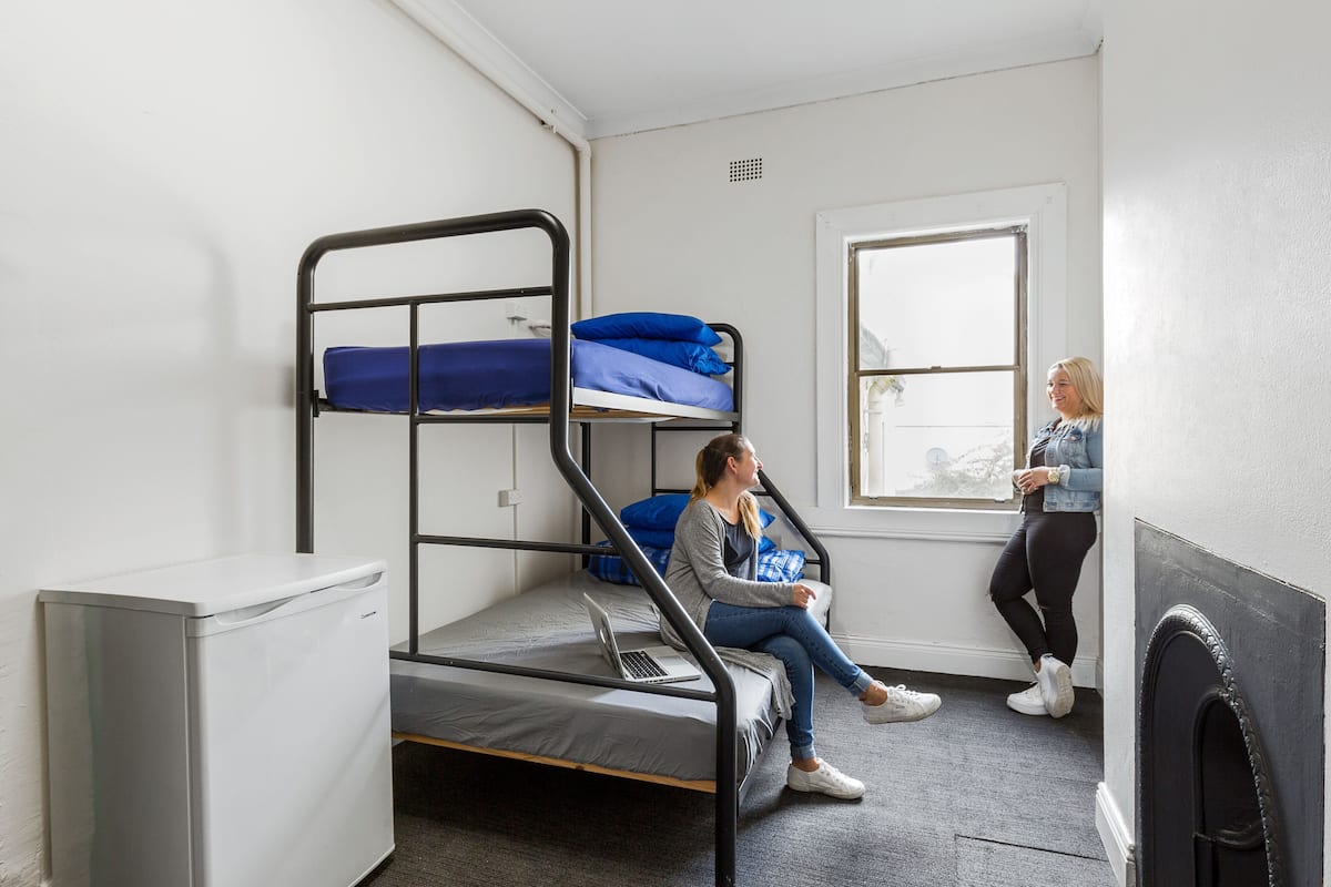 A dormitory room with bunk beds, a desk, and a window.