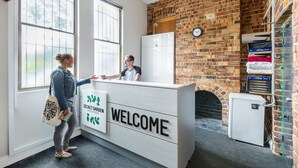 A reception area with a brick wall, a clock, and a small refrigerator. - Secret Garden Backpackers (Redfern)