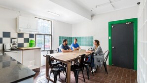 A modern kitchen with a wooden table and black chairs, a window, and a green door. - Secret Garden Backpackers (Redfern)