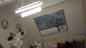 A living room with a white sofa, a clock, a lamp, and a framed picture of a snowy landscape. - Haven Suite at Jazz (Makati)