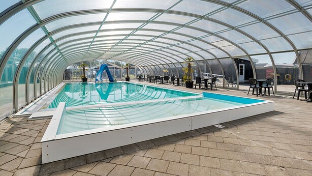 A covered swimming pool with a glass ceiling, surrounded by chairs and tables. - First Camp Holbæk Fjord (Holbaek)