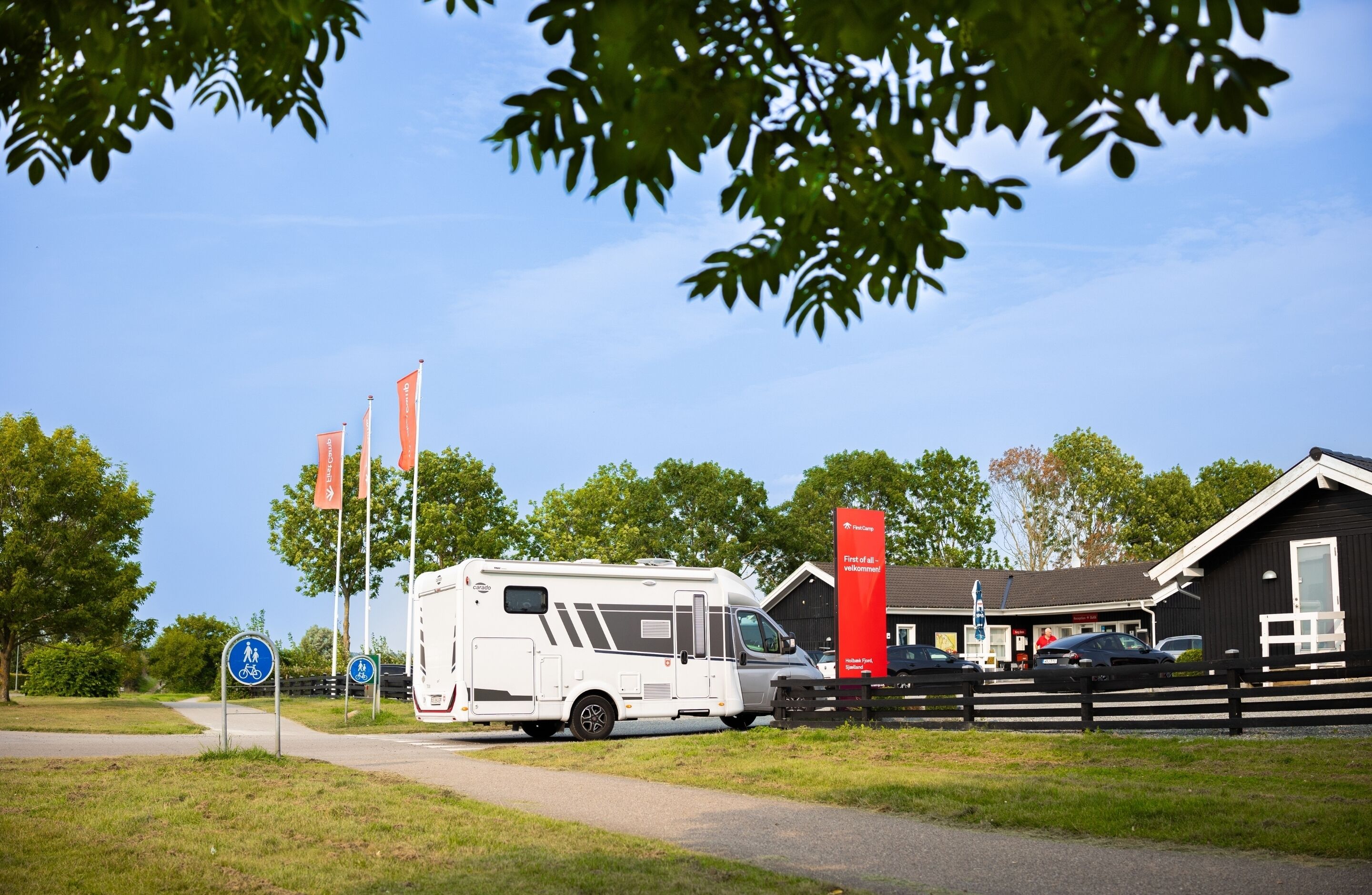 Un camping con una caravana blanca, un letrero rojo y un edificio negro.