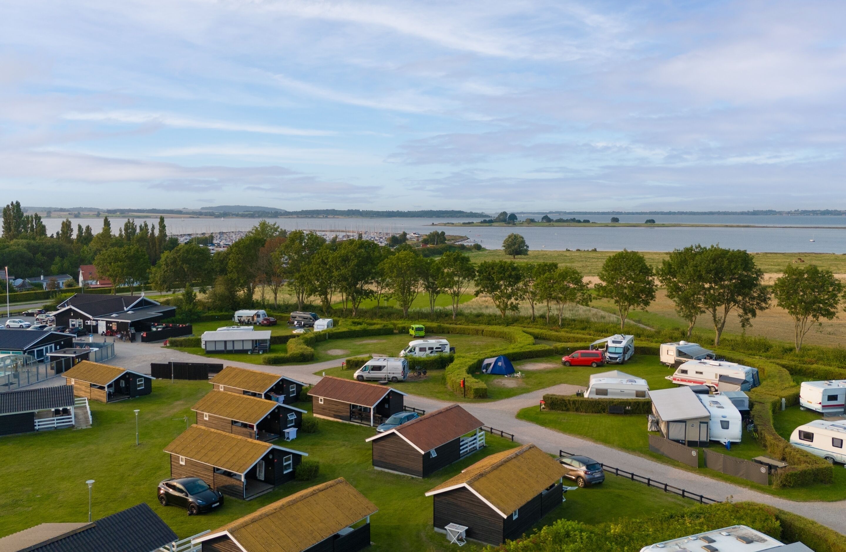 A campsite with RVs and mobile homes, a parking area, and a view of a lake.