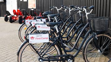 A row of bicycles with "Lejes hos First Camp" signs, parked on a cobblestone surface.