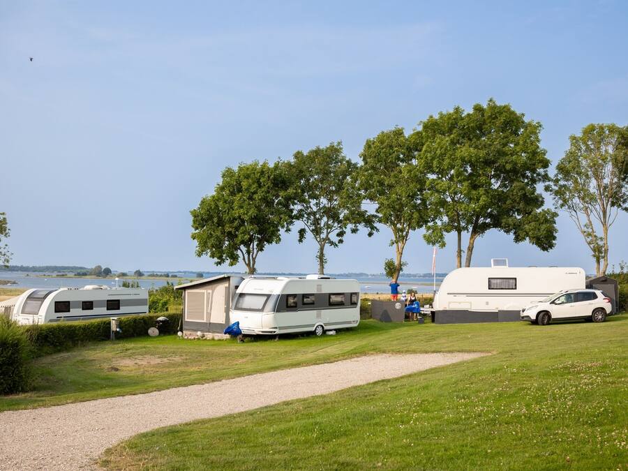 A campsite with RVs and a car parked on a grassy area near a lake.