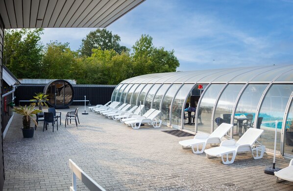 A covered outdoor area with lounge chairs and a pool.