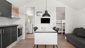 A compact kitchen with modern appliances, a dining area with a table and chairs, and a grey sofa in a bright, white-walled room. - First Camp Holbæk Fjord (Holbaek)