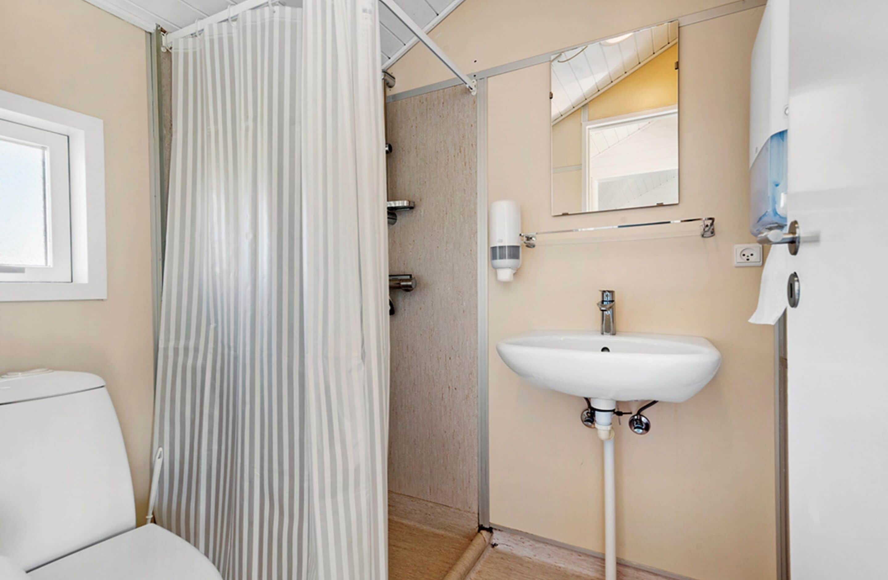 Une salle de bain avec un lavabo blanc, un miroir et un rideau de douche.