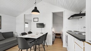 A modern kitchen with white cabinetry, a dining area with a white table and black chairs, and a gray sofa. - First Camp Holbæk Fjord (Holbaek)