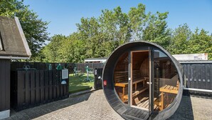 A circular wooden structure with a bench inside, a wooden fence, and a grassy area in the background. - First Camp Holbæk Fjord (Holbaek)