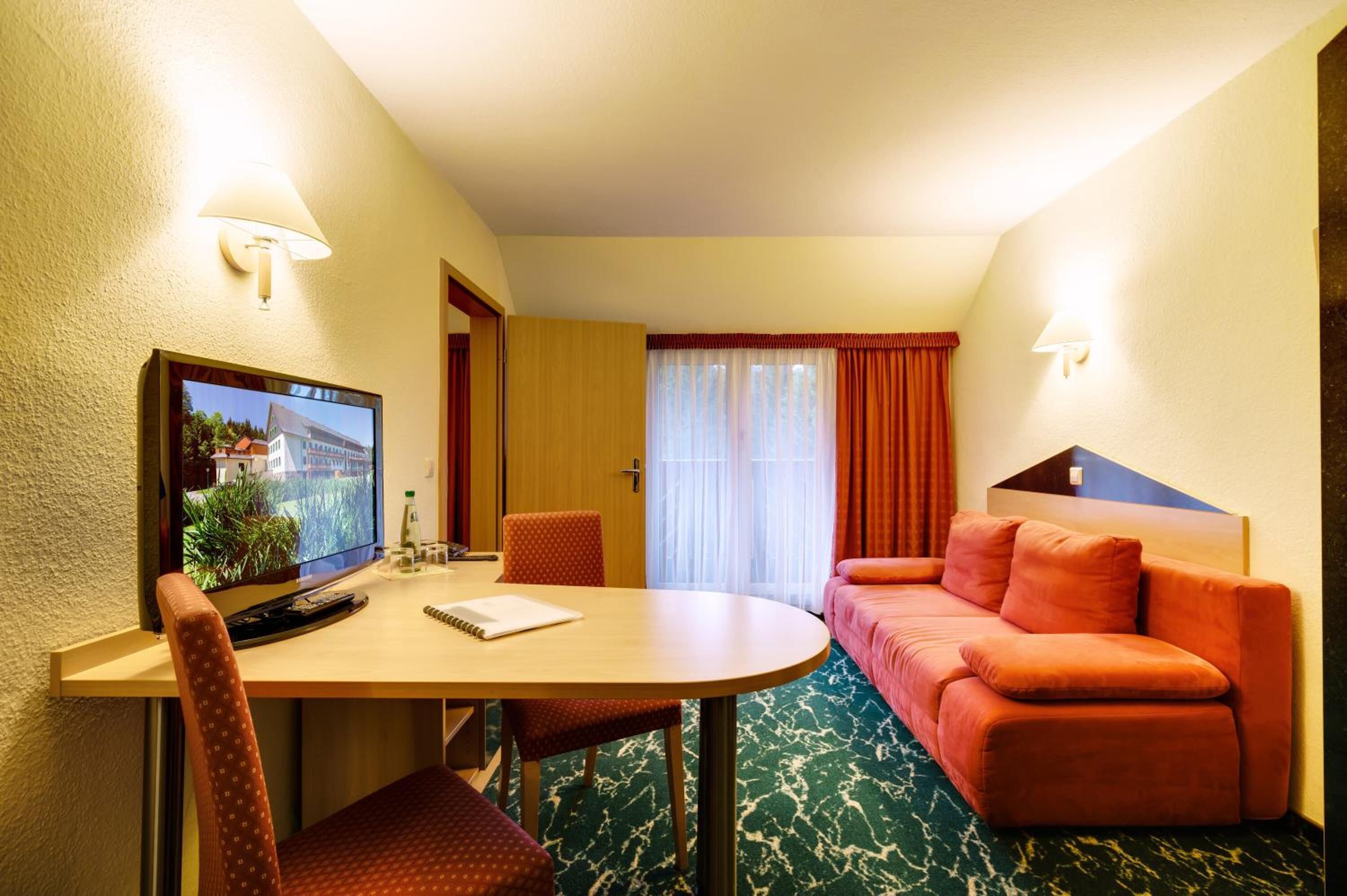 A hotel room with a round dining table, a television, a sofa, and a window with curtains.