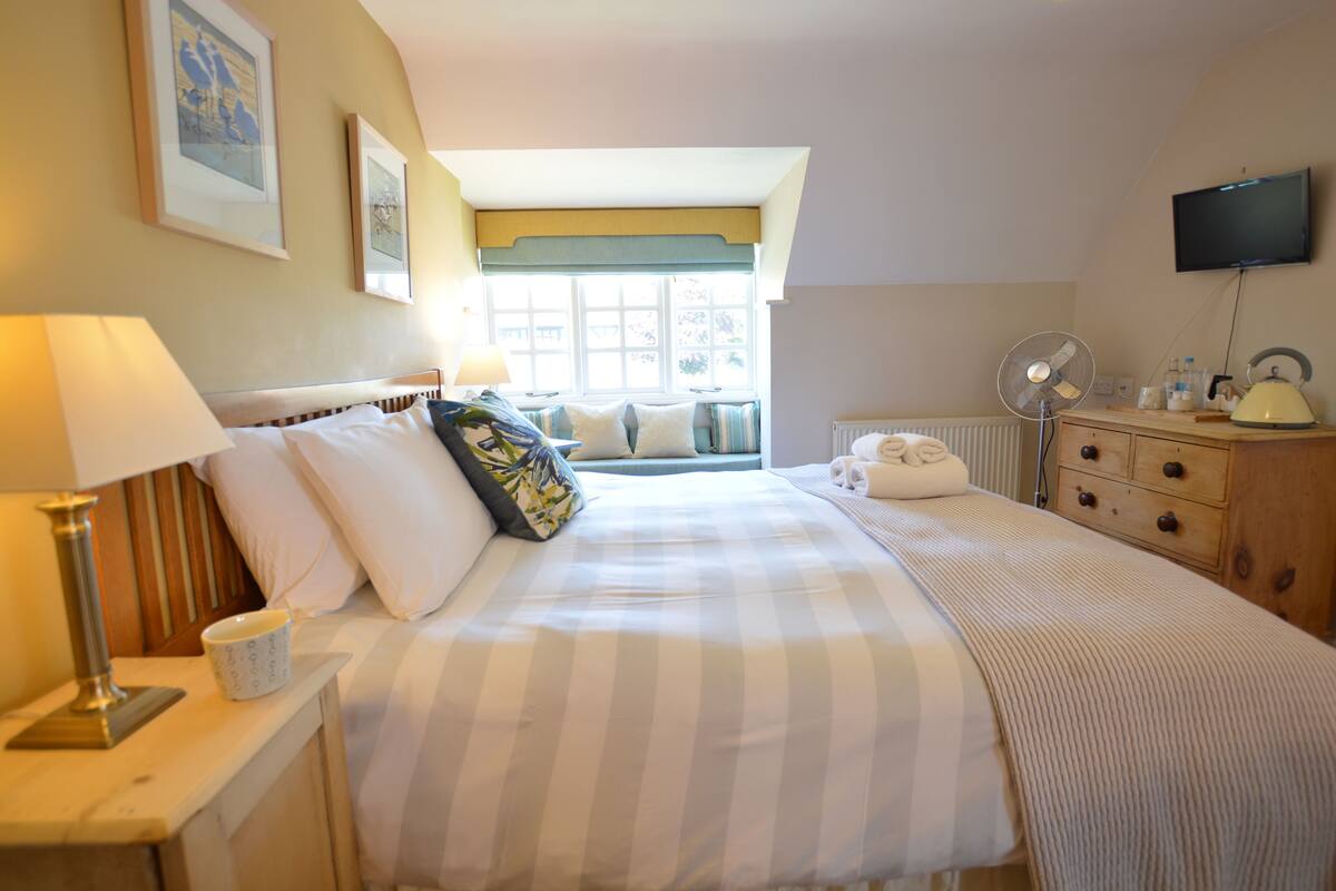 A hotel room with a bed, bedside table, lamp, and a window with a view.