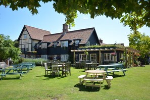 A traditional building with a tiled roof and multiple windows, surrounded by a grassy lawn with picnic tables and chairs.