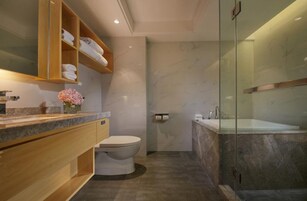 Un baño moderno con suelo de mármol, cabina de ducha de vidrio, tocador de madera con lavabo e inodoro.