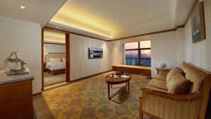 Hotelkamer met een bed, een bank, een bijzettafeltje en een groot raam met uitzicht op een zonsondergang.