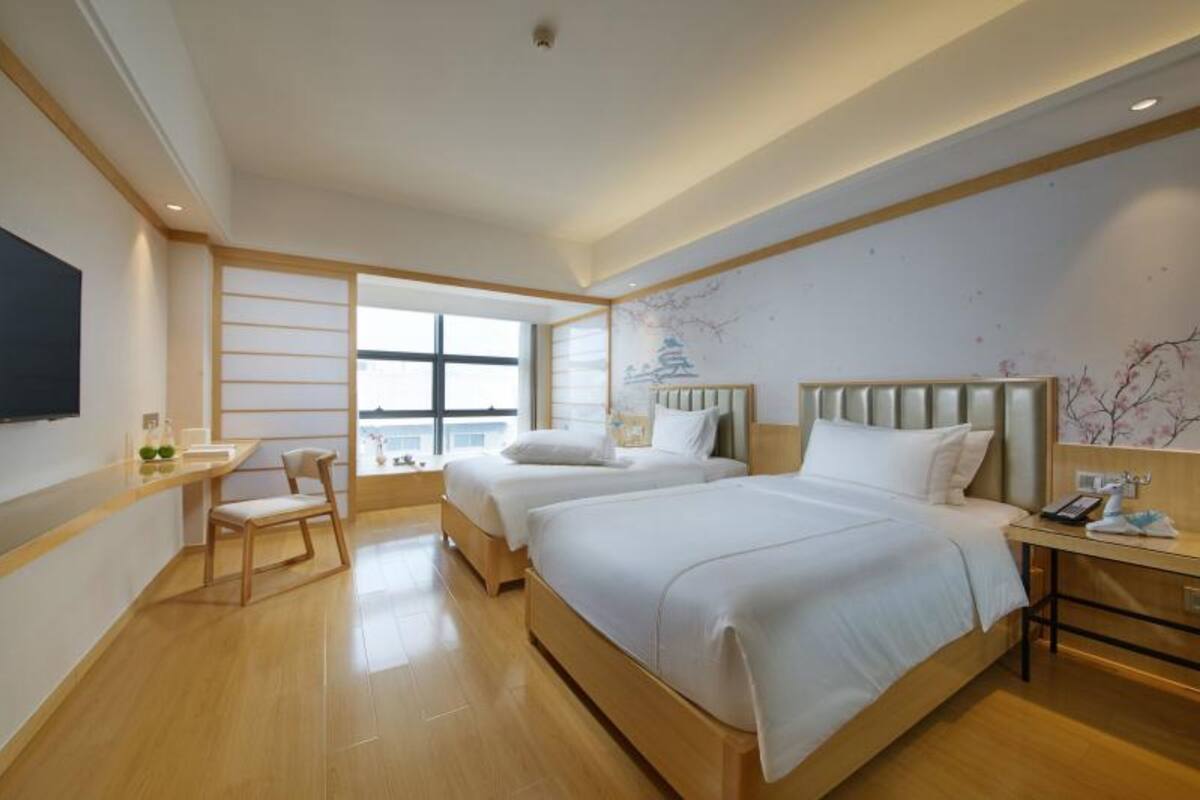 Habitación de hotel con dos camas, un escritorio, una silla y un televisor.