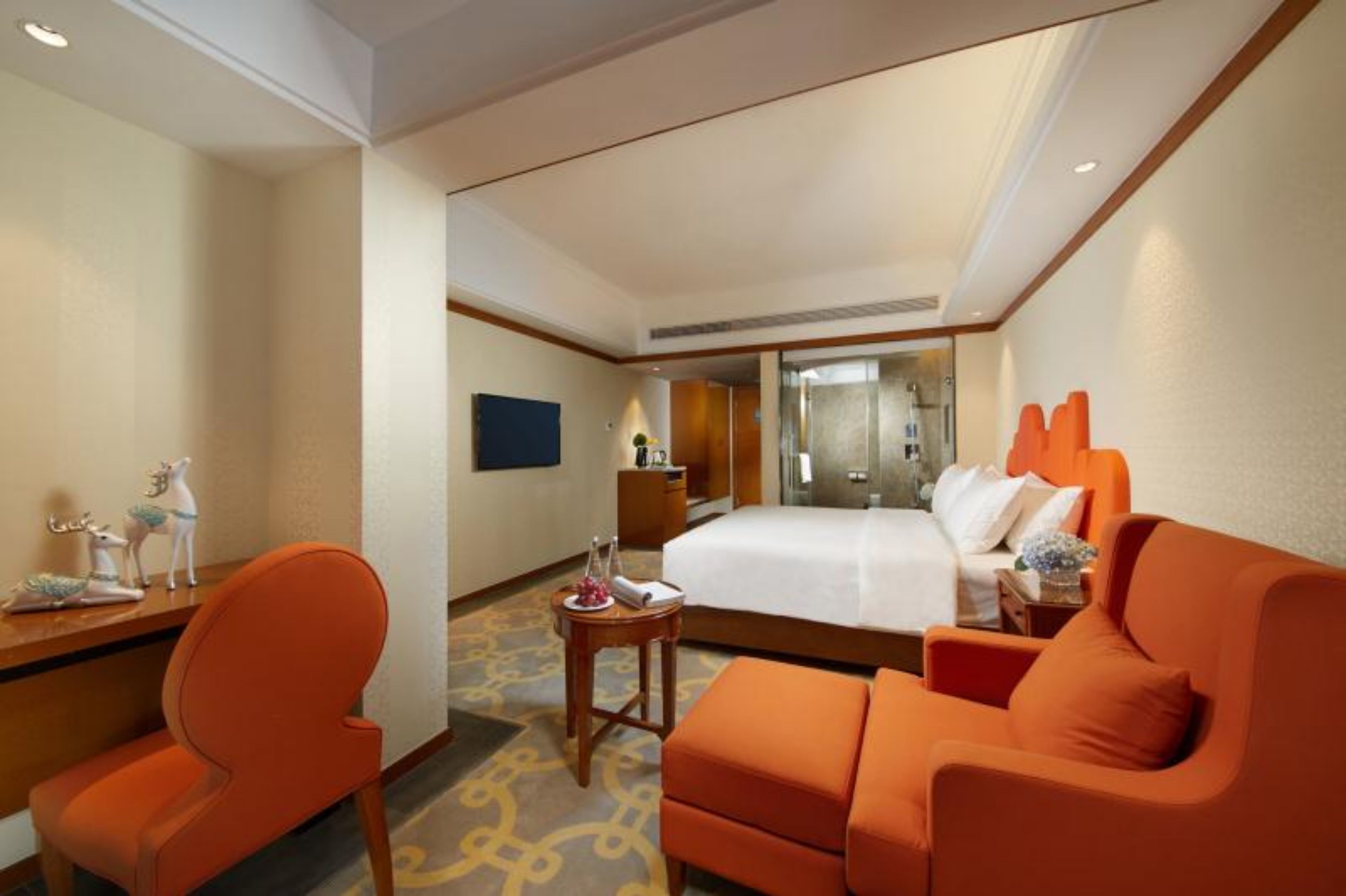 Una habitación de hotel con una cama, muebles naranjas, una mesita con un florero y un espejo.