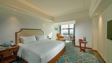 Quarto de hotel com uma cama grande, uma mesa de cabeceira, uma pequena mesa com um vaso e vista da cidade através de grandes janelas.
