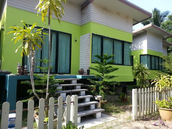 A two-story building with a green exterior, a white picket fence, and a concrete staircase leading to the entrance.